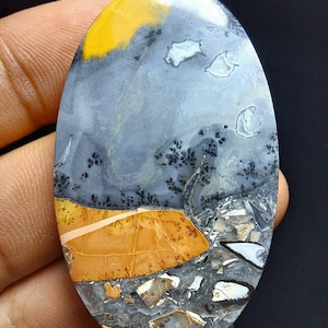 Peut inclure: Pierre précieuse ovale avec un motif de paysage. La pierre présente une palette de couleurs jaune, grise et orange avec des accents noirs. Le motif ressemble à un paysage avec un ciel, des montagnes et un premier plan.