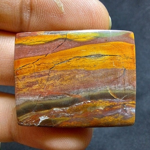 May include: A rectangular, polished, multi-coloured stone with a layered pattern of brown, orange, yellow, and red. The stone has a natural, rough edge.