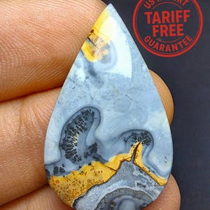 May include: A pear-shaped gemstone displaying a distinctive pattern. The stone combines light blue, yellow, and grey tones, with detailed veining and speckled features. The top section of the stone is bright yellow, fading into a light blue background.