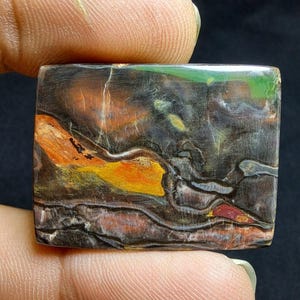 May include: A rectangular gemstone with a unique pattern of colours. The stone features a blend of brown, orange, yellow, green, and red hues. The polished surface showcases a natural, layered design, with a dark background.