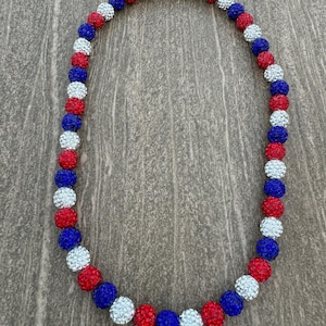 May include: A red, white, and blue beaded necklace with a patriotic theme. The beads are small and round, and they are arranged in a repeating pattern of red, white, and blue.