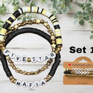 May include: Set of three bracelets with black and white beads and gold stars. The bracelets spell out "Five Star Mafia" in white letters on black beads.