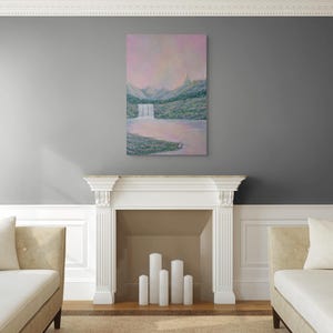 May include: An oil painting of a waterfall cascading into a lake, set against a backdrop of mountains and a pink sky. The artwork is displayed above a white fireplace, flanked by two beige chaise lounges.
