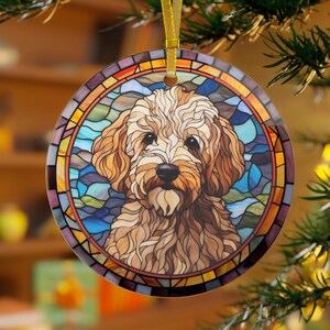 May include: Round Christmas ornament featuring a dog in a stained-glass style design. The dog has brown fur and a black nose, set against a backdrop of blue, green, and orange glass. A gold ribbon is attached for hanging.