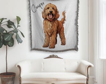 May include: A light gray throw blanket with a fringed edge, featuring a drawing of a golden doodle dog. The dog is standing with its tongue out, wearing a red collar. The name "Cooper" is written above the dog in cursive.