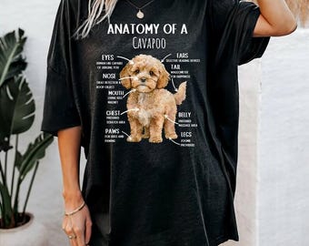May include: A black short-sleeved t-shirt featuring a graphic of a light brown Cavapoo puppy. The text reads Anatomy of a Cavapoo with labels pointing to the puppy's body parts, including eyes, ears, nose, tail, mouth, chest, belly, paws, and legs.