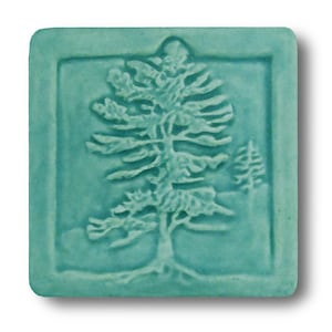 以下が含まれることがあります： ターコイズブルーのセラミックタイルに、松の木のレリーフデザインが施されています。木はタイルの中央にあり、縁取りで囲まれています。
