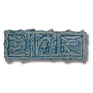 May include: A blue ceramic tile featuring a raised design of a beaver, trees, and a mountain scene.