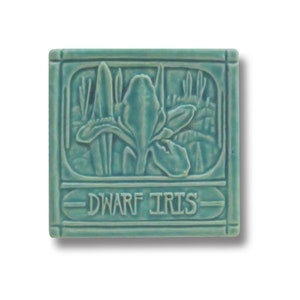 May include: A teal blue ceramic tile with a raised image of a dwarf iris flower. The tile has a border and the words "DWARF IRIS" are written below the image.