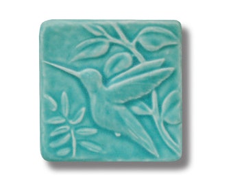 May include: A turquoise ceramic tile with a raised design of a hummingbird in flight, surrounded by leaves.