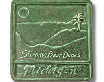 Puede incluir: Un azulejo de cerámica verde con una imagen en relieve de un paisaje con un árbol y las palabras "Sleeping Bear Dunes Michigan".