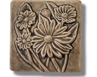 May include: A ceramic tile with a raised design of brown flowers. The flowers are in a cluster and have a detailed, realistic look.