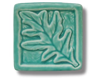 May include: A teal blue ceramic tile with a raised design of an oak leaf.