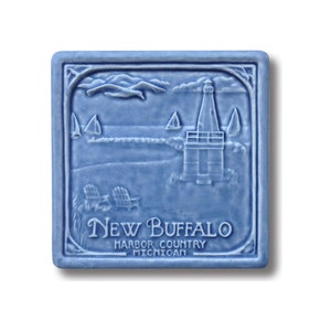 May include: A blue ceramic tile with a raised image of a lighthouse, sailboats, and a beach scene. The tile has the text "New Buffalo Harbor Country Michigan" in white.