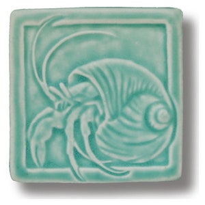 May include: A ceramic tile with a raised design of a hermit crab in a shell. The tile is a light teal color.