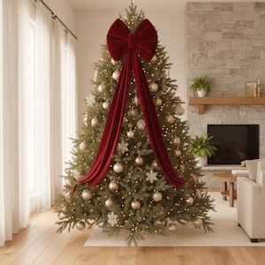 May include: A large, deep red velvet bow with two long, flowing tails draped down the front of a green Christmas tree. The tree is decorated with numerous round, metallic gold ornaments and white snowflake accents, illuminated by warm string lights.