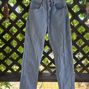 May include: High-waisted light wash denim jeans featuring a classic five-pocket design, a button fly closure, and straight legs. The denim has a faded blue appearance with visible stitching along the side seams and a structured waistband.