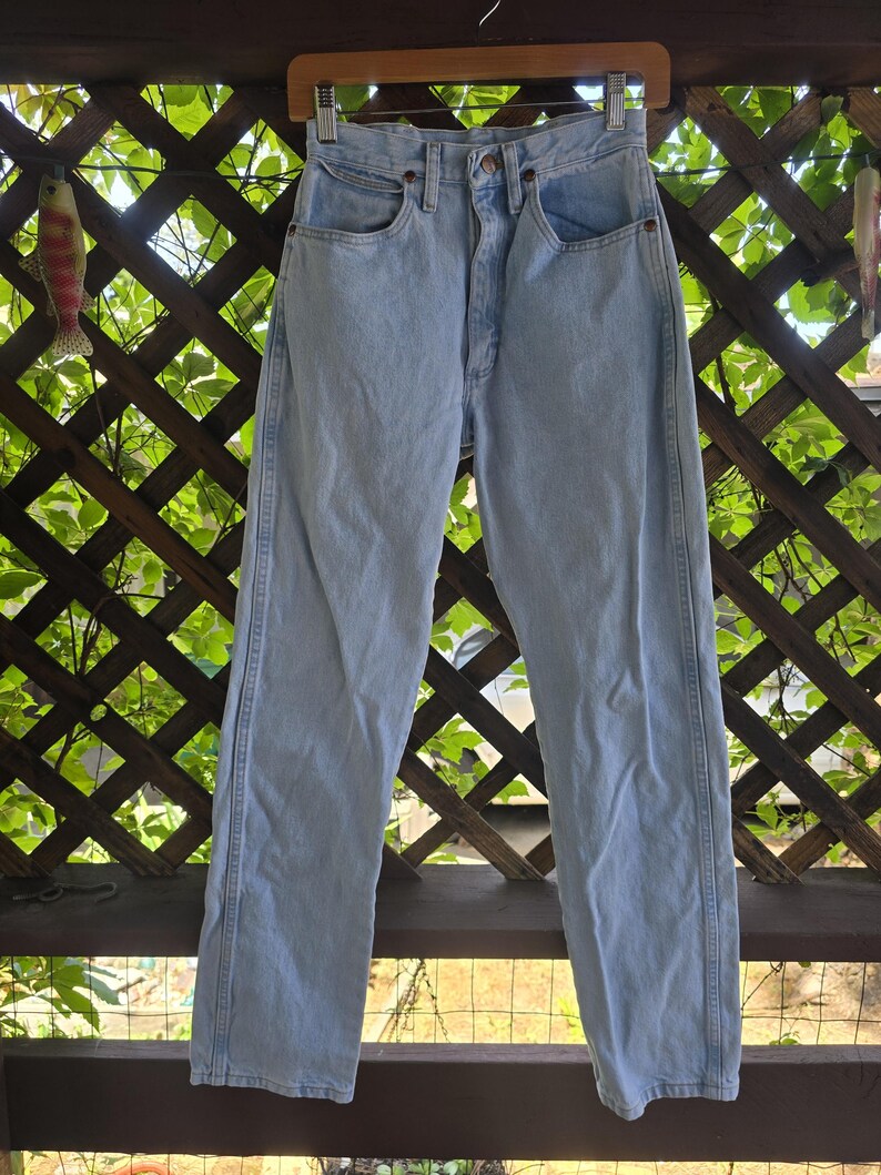 May include: High-waisted light wash denim jeans featuring a classic five-pocket design, a button fly closure, and straight legs. The denim has a faded blue appearance with visible stitching along the side seams and a structured waistband.