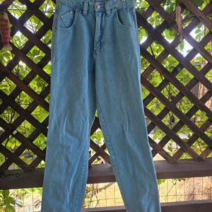 May include: Light blue high-waisted denim jeans featuring a classic five-pocket design, a metal button closure, a zippered fly, and belt loops. The pants have a straight-leg cut with visible stitching details along the pockets and waistband.