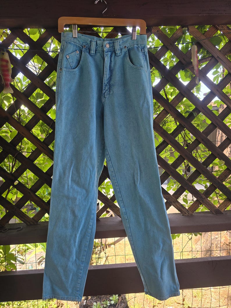 May include: Light blue high-waisted denim jeans featuring a classic five-pocket design, a metal button closure, a zippered fly, and belt loops. The pants have a straight-leg cut with visible stitching details along the pockets and waistband.