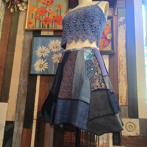 May include: A blue lace crop top with a single strap and a patchwork denim skirt. The skirt features various denim washes and patterned fabric panels. The outfit is displayed on a mannequin.