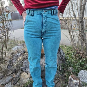 May include: High-waisted light blue denim jeans with a button fly and a belt loop detail. The jeans have a faded, distressed look.