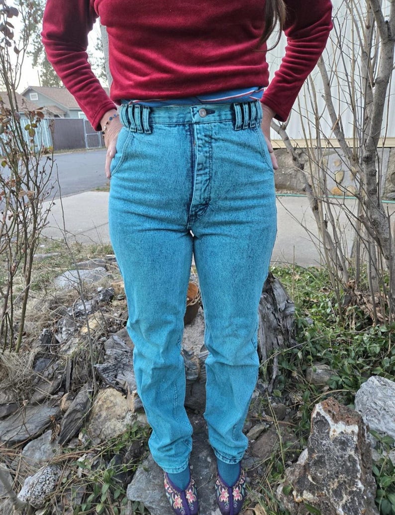 May include: High-waisted light blue denim jeans with a button fly and a belt loop detail. The jeans have a faded, distressed look.