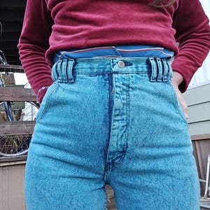 May include: High-waisted blue denim jeans with a light blue acid wash. The jeans have a button fly and a belt loop detail.