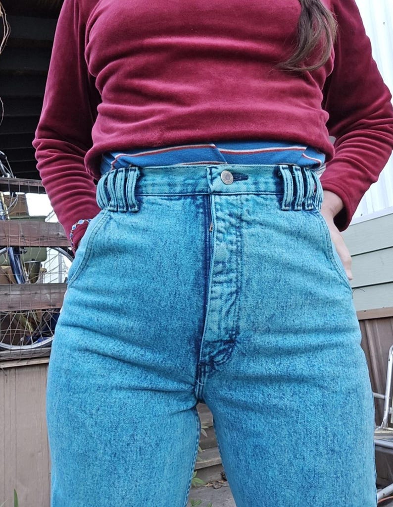 May include: High-waisted blue denim jeans with a light blue acid wash. The jeans have a button fly and a belt loop detail.