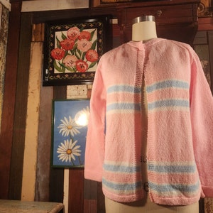 May include: A pink knitted cardigan with blue and white stripes. The cardigan has a button-up front and long sleeves.
