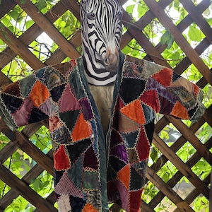 May include: A patchwork jacket constructed from various triangular pieces of velvet fabric in shades of orange, purple, black, green, and blue. The pieces are joined together with visible white zigzag stitching along the seams.