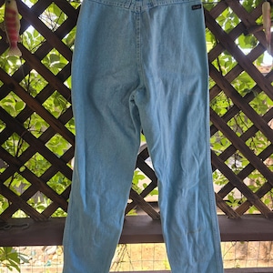 May include: Light blue denim jeans featuring a high-waisted design with a back yoke, belt loops, and a small black brand tag on the right side. The pants have a straight-leg cut, a classic five-pocket construction, and a light wash finish.