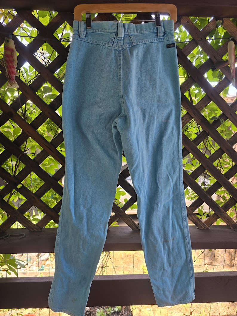 May include: Light blue denim jeans featuring a high-waisted design with a back yoke, belt loops, and a small black brand tag on the right side. The pants have a straight-leg cut, a classic five-pocket construction, and a light wash finish.