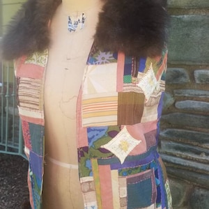 May include: A patchwork vest with a brown faux fur collar. The vest is made of different fabrics in various colors, including pink, green, blue, and brown. The vest is on a dress form.
