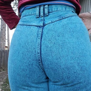 May include: A pair of high-waisted blue jeans with a light blue acid wash finish. The jeans have a back pocket detail with two vertical seams.