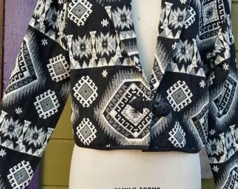 May include: Black and white cropped jacket with a geometric pattern. The jacket has a button closure and a collar. The label on the jacket reads "Family Forms 8 Collapsible".