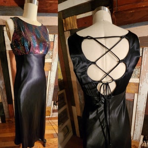 Könnte beinhalten: Ein schwarzes Satin-Kleid mit einem Pailletten-Oberteil und einem Schnürrücken. Das Kleid hat ein figurbetontes Oberteil und einen fließenden Rock.