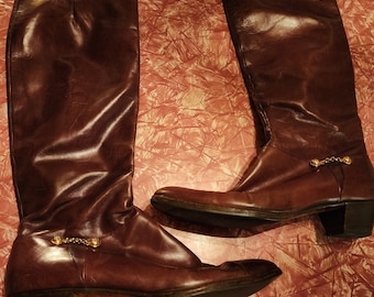 May include: A pair of brown leather knee-high boots with gold chain accents and a block heel.