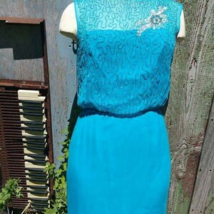 May include: A turquoise sleeveless dress with a beaded top and a silver brooch. The dress has a fitted bodice and a flowing skirt.