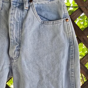 May include: Light blue denim jeans featuring a high-waisted design with a button fly closure, copper-toned metal rivets at the pocket corners, and a classic five-pocket construction. The fabric has a light wash finish with visible stitching.