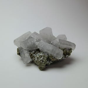 May include: A cluster of clear, crystalline quartz formations atop a matrix of pyrite. The quartz crystals are elongated and translucent, with a slightly frosted appearance. The pyrite base has a metallic, golden sheen.