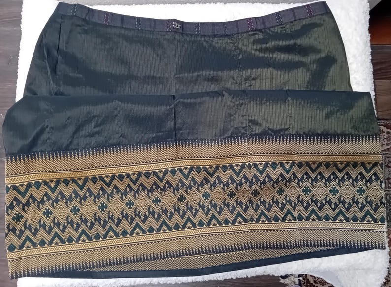 May include: A black skirt with a gold and green patterned trim. The skirt is made of a silky fabric and has a waistband.