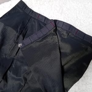 May include: Black skirt with a zipper closure and a plaid lining. The skirt is made of a smooth, silky fabric.