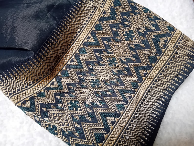 May include: Black fabric with a gold and green geometric pattern. The pattern is woven into the fabric and features a variety of shapes, including squares, triangles, and diamonds.
