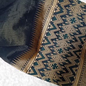 May include: Black fabric with a gold and green patterned border. The pattern is geometric and features a repeating design of triangles and squares.