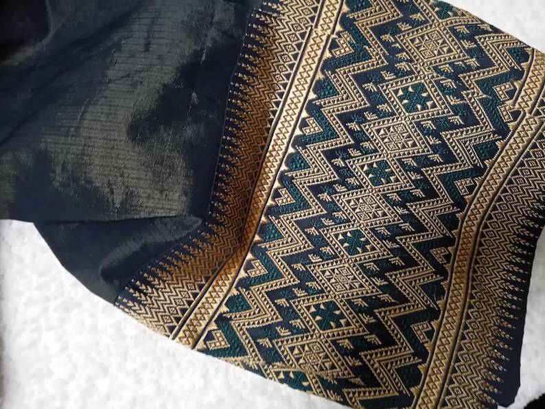 May include: Black fabric with a gold and green patterned border. The pattern is geometric and features a repeating design of triangles and squares.