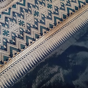 May include: A close-up of a dark blue fabric with a gold and green geometric pattern. The fabric has a woven texture and a subtle sheen.
