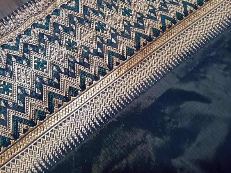 May include: A close-up of a dark blue fabric with a gold and green geometric pattern. The fabric has a woven texture and a subtle sheen.