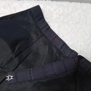 May include: Black skirt with a plaid waistband and a black fabric belt with a silver buckle. The skirt has a pleated design.