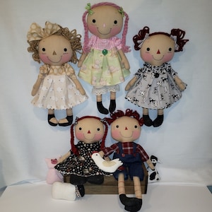 May include: Five handmade rag dolls with different colored hair and clothing. The dolls are wearing dresses and overalls. Two of the dolls are holding a small toy chicken and a pig.